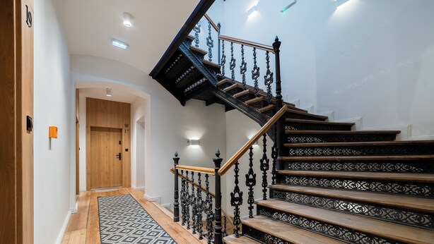 A staircase with ornate black balusters and wooden steps, leading to a landing with a patterned rug and a wooden door.