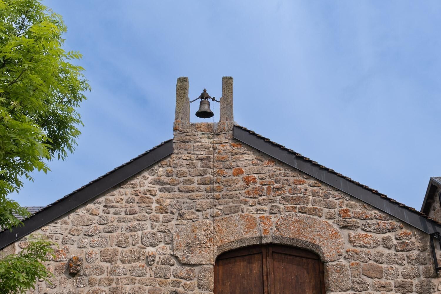 A stone building with a bell tower, a wooden door, and a clear sky.