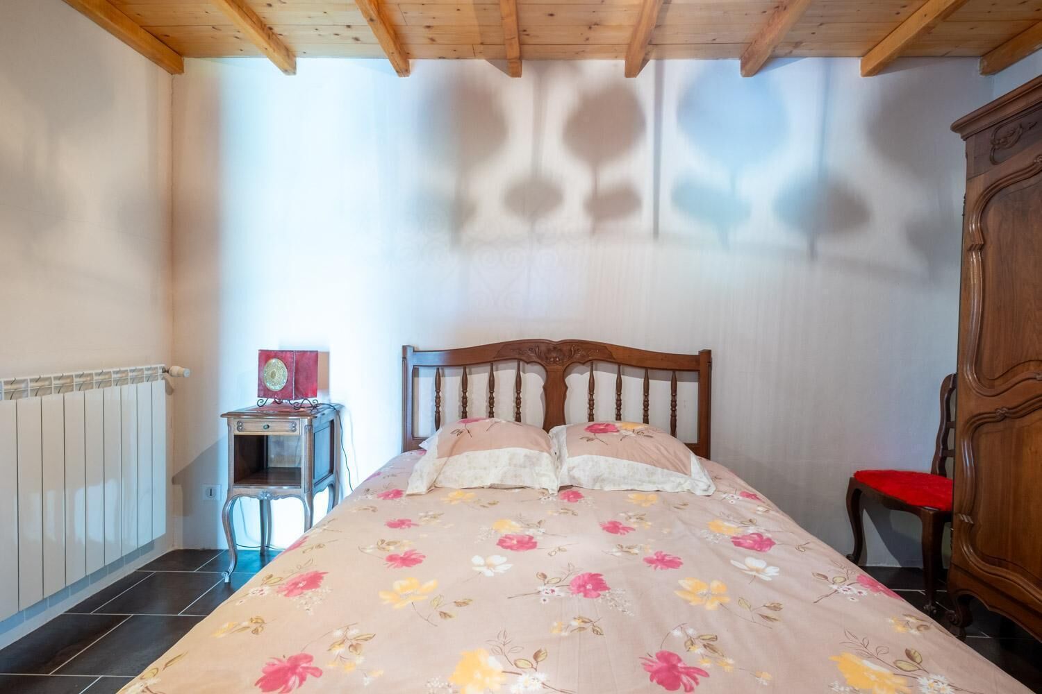A bedroom with a wooden bed, a nightstand, a red chair, and a radiator.