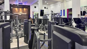 Un gimnasio moderno con diversos equipos de ejercicio, un espejo grande y una pantalla digital en la pared.