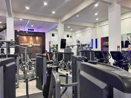 Un gimnasio moderno con diversos equipos de ejercicio, un espejo grande y una pantalla digital en la pared.