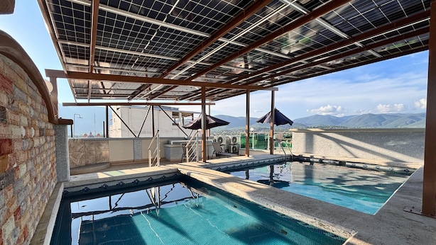 Una piscina en la azotea con vistas a montañas, paneles solares y mobiliario exterior.