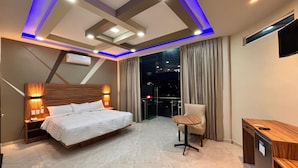 Una habitación de hotel moderna con una cama grande, un escritorio y una silla. Se ve la ciudad iluminada desde la ventana.
