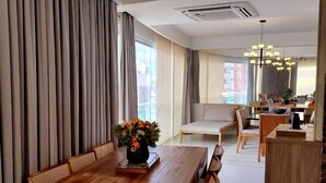 A spacious dining area with a wooden table and chairs, a vase of flowers, and a view of the city through large windows. - Charming Apartment (Belém)