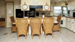 Une cuisine avec des chaises en osier, une horloge et un panneau d’accueil.