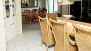 Un coin repas avec des chaises en osier, une table en bois et une cuisine équipée d’une cuisinière.