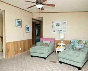 A room with two green upholstered sofas, a ceiling fan, framed pictures on the walls, and a small white table with books.