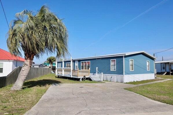 Een gelijkvloers huis met een veranda, een palmboom en een helderblauwe lucht.
