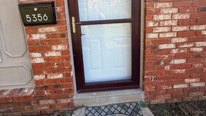 A residential entrance with a brick wall, a dark wooden door, and a welcome mat. - Emmanuel Midtown 2 BR 1.5 Bath Condo in Tulsa. Close to YMCA, Hospitals, Highway (Tulsa)