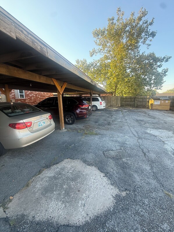 A parking area with two cars under a wooden structure, a brick wall, and a tree. - Emmanuel Midtown 2 BR 1.5 Bath Condo in Tulsa. Close to YMCA, Hospitals, Highway (Tulsa)