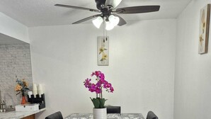 A dining area with a table set for four, a ceiling fan, and a kitchen area with a brick backsplash and a bar. - Emmanuel Midtown 2 BR 1.5 Bath Condo in Tulsa. Close to YMCA, Hospitals, Highway (Tulsa)