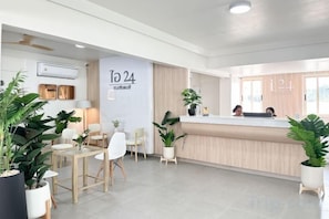 Un espace d’accueil comprenant un comptoir de réception, des chaises, des plantes en pot et un mur orné du chiffre « 24 » et d’un logo.
