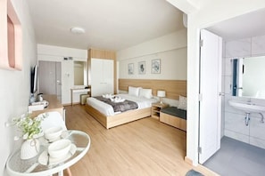 Ett modernt hotellrum med en säng, ett nattduksbord och ett badrum med handfat och spegel.
