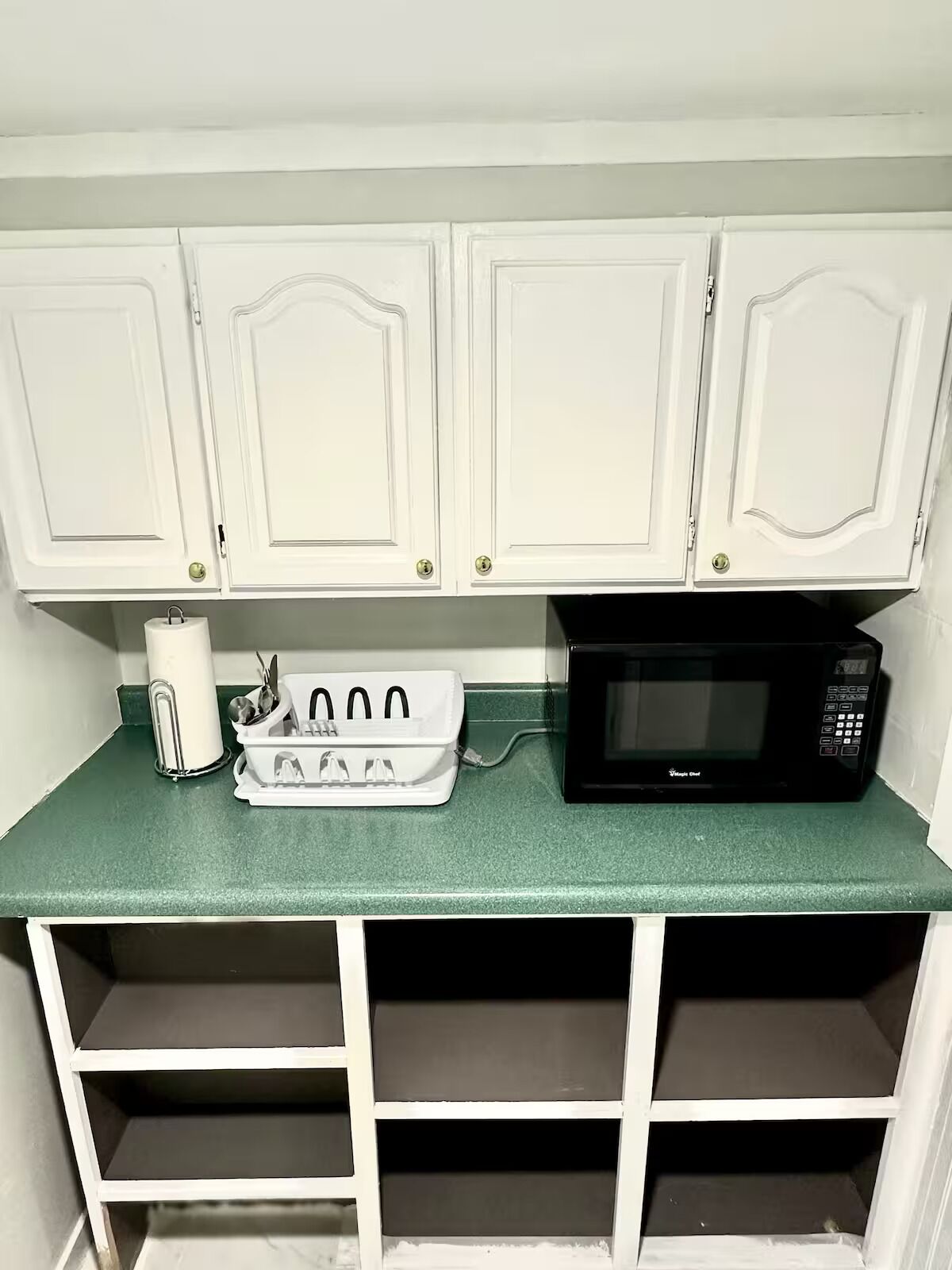 A kitchen with white cabinets, a green countertop, a white dish rack, and a black microwave.