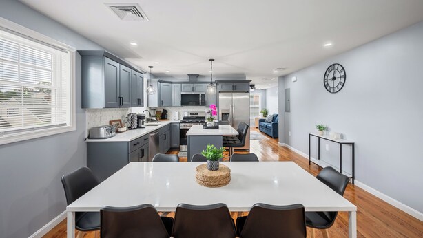 A modern kitchen with grey cabinets, a central island, and a dining area with a white table and black chairs.