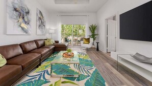 A modern living room with a brown leather sofa, a glass coffee table, and a large abstract painting on the wall. - Seven Eagles Springs: Near Disney, Golf, Free Water Park (Kissimmee)