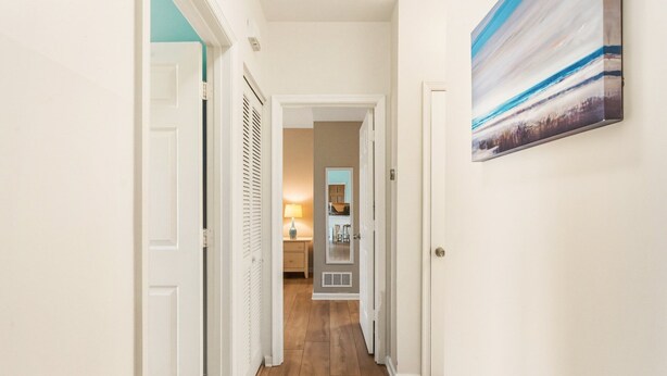 A hallway with wooden flooring, white walls, and a view into a room with a kitchen area. - Walk to Beach! Poolside Coastal Condo Retreat (Kill Devil Hills)