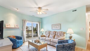 A living room with a sofa, armchair, coffee table, and a television. - Walk to Beach! Poolside Coastal Condo Retreat (Kill Devil Hills)