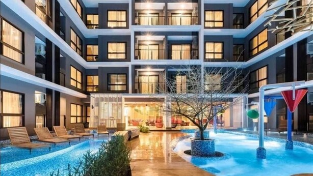 Un hotel de varios pisos con un patio central que cuenta con una piscina, sillas de descanso y un área de estar.