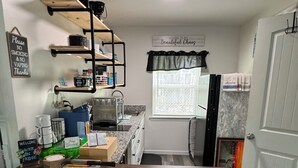 A kitchen with a wooden table, bar stools, a coffee machine, and shelves with various items.
