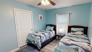 A bedroom with two single beds, a door, a window with blinds, and a ceiling fan.