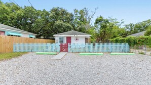 A small house with a red door, a blue picket fence, and a gravel driveway.