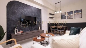 A modern living room with a flat-screen TV, a dark marble accent wall, a dining area with a wooden table and chairs, and a cozy seating area with a white sofa and fluffy pillows. - EduSentral Premier Suites Setia Alam (Shah Alam)