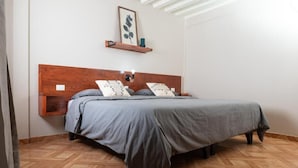 Ein Schlafzimmer mit einem Holzkopfende, einem Bett mit grauer Bettwäsche, einem an der Wand befestigten Regal mit einer Pflanze und einem Fischgrätparkett.