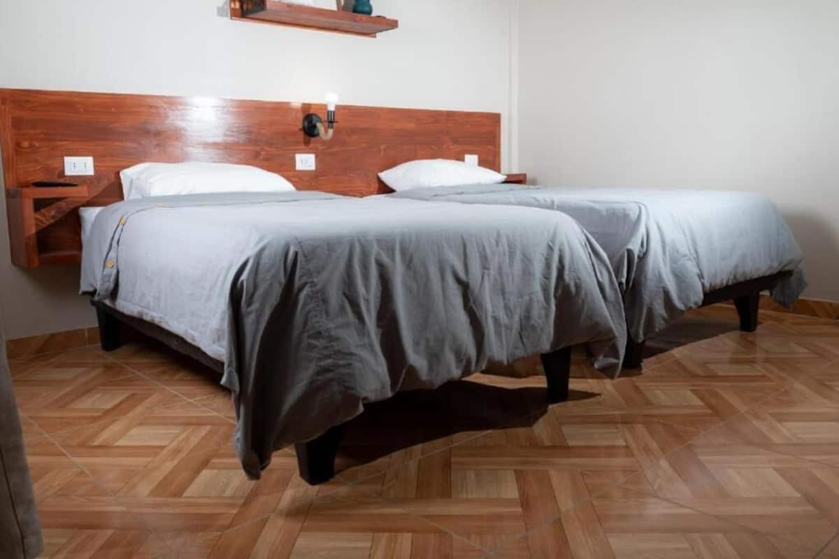 Una habitación con dos camas, cabeceros de madera y un suelo con estampado de espiga.