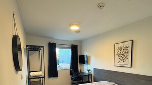 A hotel room with a bed, a desk, a chair, a TV, a window with curtains, a radiator, and a framed botanical print on the wall. - 248 Halls (Middlesbrough)