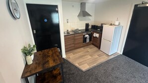 A compact kitchen with a black door, a clock, a small table with a plant, and a microwave. - 248 Halls (Middlesbrough)