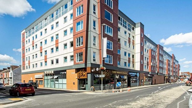 A multi-story hotel with a modern design, featuring a mix of red and white exterior panels, multiple windows, and ground-level retail spaces. - 248 Halls (Middlesbrough)
