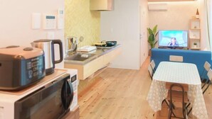 Een praktische keuken met een magnetron, waterkoker en een klein eethoekje met een tafel en stoelen.