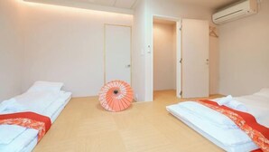 Een hotelkamer met twee bedden, een houten vloer, een airconditioningsysteem en een open deur die leidt naar een andere kamer.