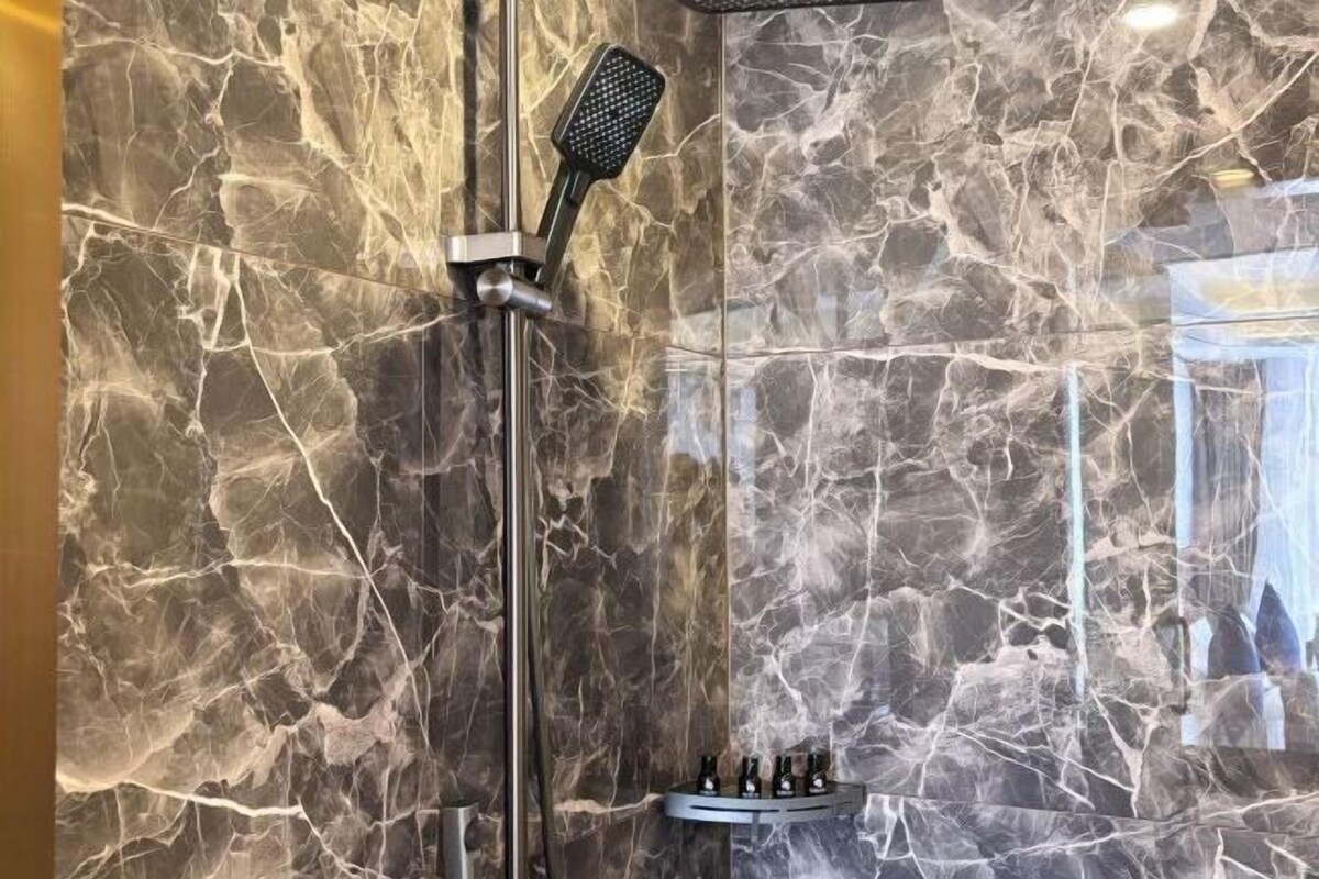 Een douche met een handdouche, een marmeren wand en een plank met flesjes.
