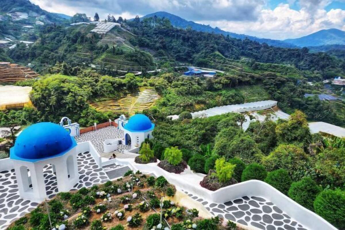 Un giardino a terrazze con strutture bianche e blu, vegetazione lussureggiante e un paesaggio montuoso sullo sfondo.