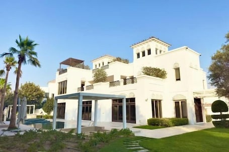 A white multi-story building with balconies, a covered outdoor seating area, and a swimming pool.