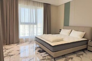 A bedroom with a bed, curtains, a nightstand, and a marble floor. - jinnuo vacation home (Dubai)