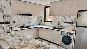 Cozinha moderna com bancadas de mármore, máquina de lavar embutida e janela.