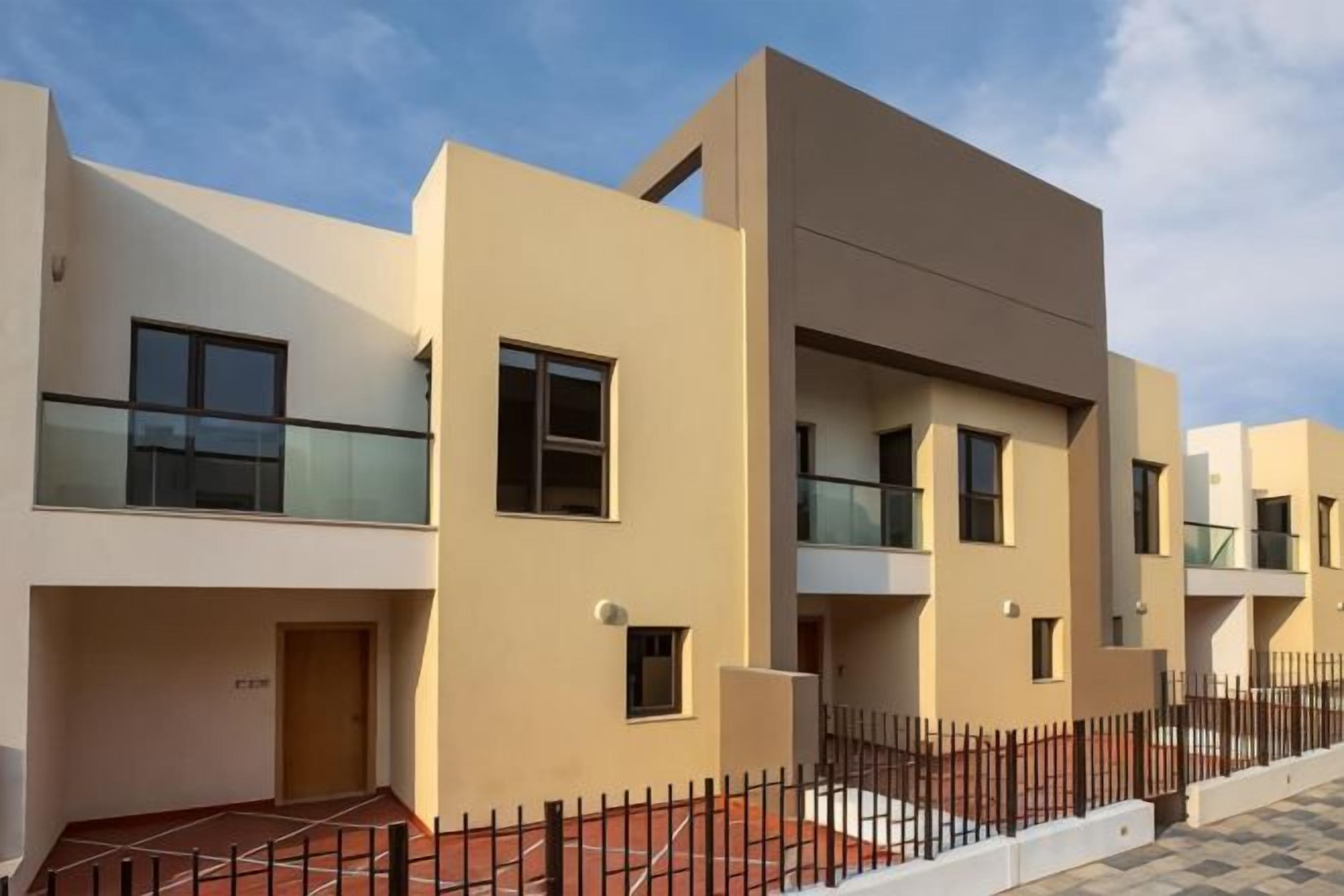 A modern multi-story residential building with balconies, a gated entrance, and a clear sky.