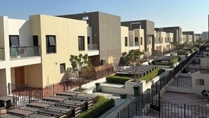 Uma fileira de edifícios residenciais modernos com varandas, um pátio central com vegetação e céu claro.
