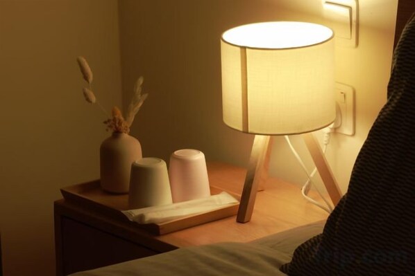 A bedside table with a lamp, a vase with dried flowers, and two candles.