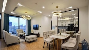 A modern hotel room with a dining area, a large window with a city view, and a chandelier. - Vinhomes Metropolis Apartment - Comfort Stay Ha Noi (Hanoi)