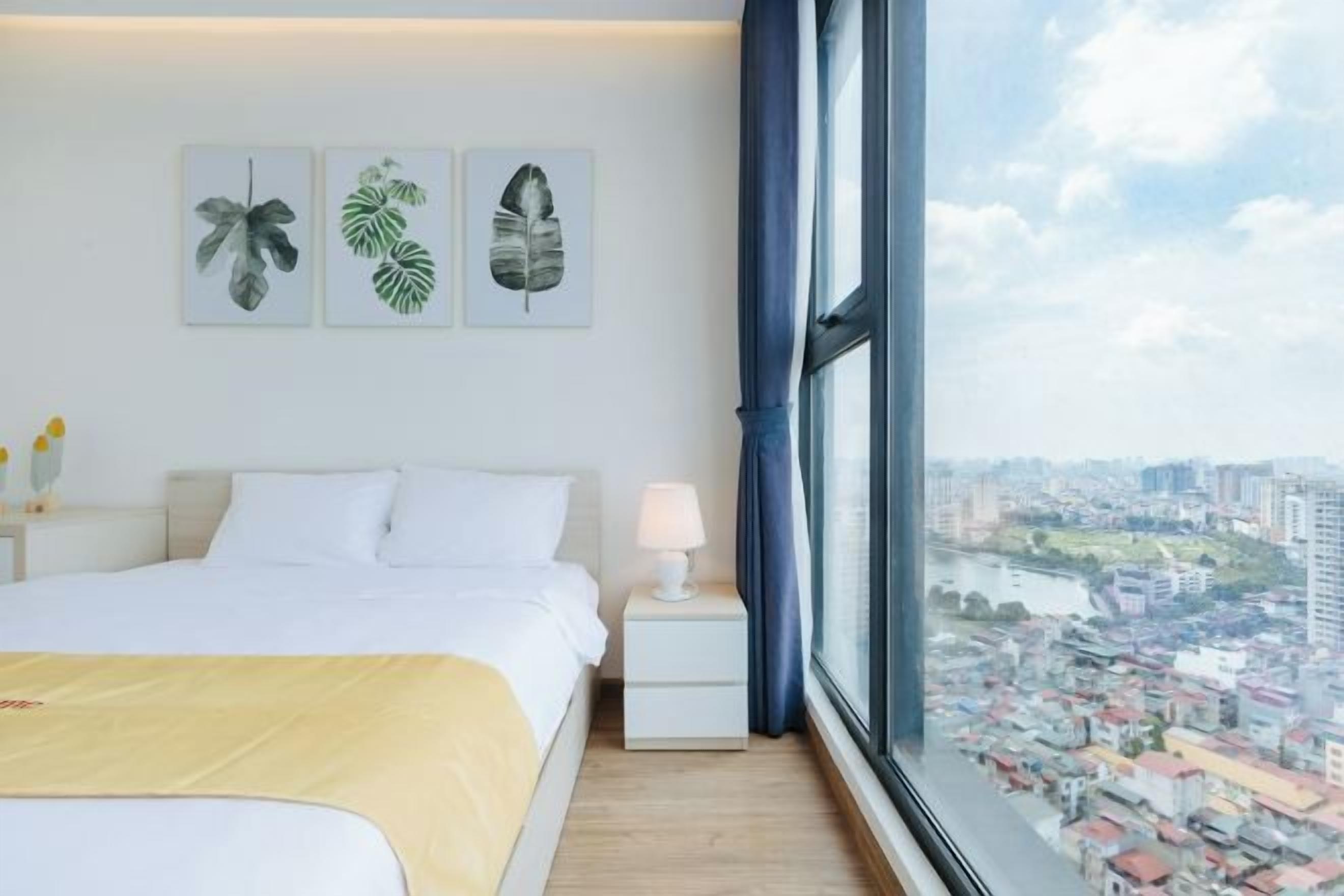 A hotel room with a large bed, a nightstand, a lamp, and a window with a city view.