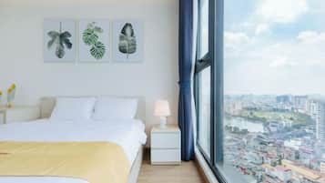 A hotel room with a large bed, a nightstand, a lamp, and a window with a city view.