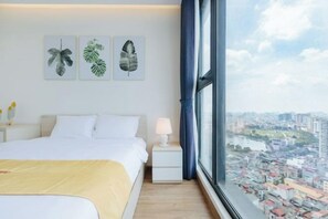 A hotel room with a large bed, a nightstand, a lamp, and a window with a city view. - Vinhomes Metropolis Apartment - Comfort Stay Ha Noi (Hanoi)