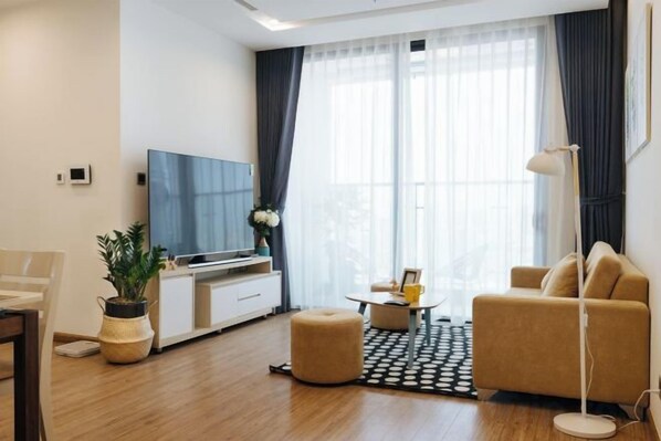 A modern living room with a flat-screen TV, a sofa, a coffee table, and a potted plant. - Vinhomes Metropolis Apartment - Comfort Stay Ha Noi (Hanoi)