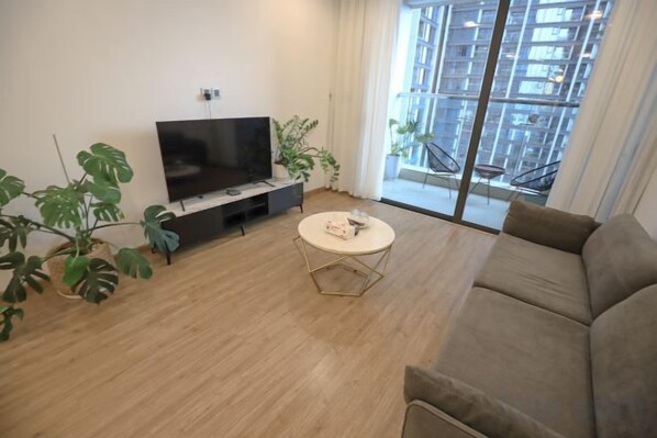A living room with a flat-screen TV, a round coffee table, a sofa, and a large window with a view of buildings. - Vinhomes Metropolis Apartment - Comfort Stay Ha Noi (Hanoi)