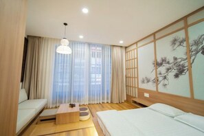 Una habitación de hotel con cama, sofá, una mesita y un ventanal con cortinas.