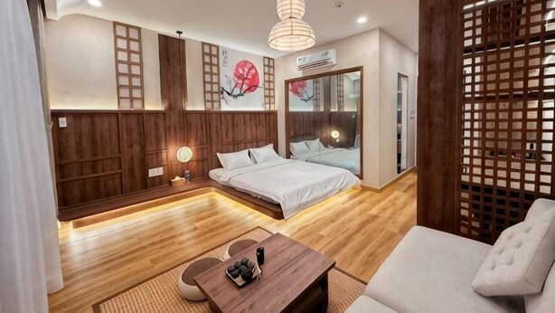A modern hotel room with a bed, a sofa, a wooden floor, a desk, and a large window. - KATOYA SUITES SAIGON HONKAN (Ho Chi Minh City)